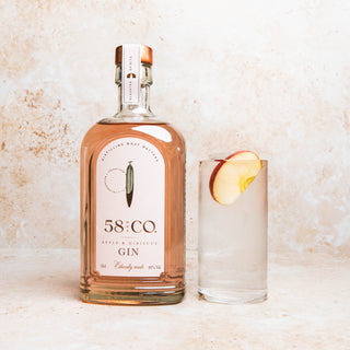 Bottle of 58 and CO Apple and Hibiscus Pink Gin with a glass of gin and apple slice on a textured surface