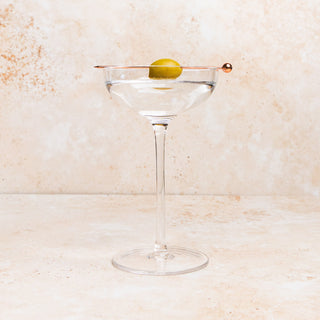 Clear martini glass with a olive on a light stone background