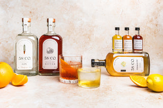 The negroni collection - Bottles of 58 CO spirits with glasses of negroni cocktails on a light background