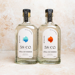 Two bottles of 58 and CO Olive Oil Vodka, one labeled Greece and the other Spain, against a textured background.