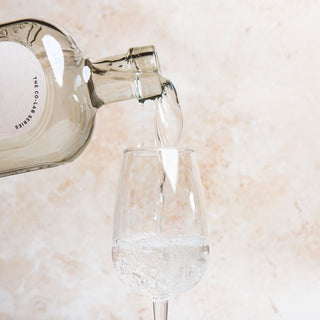 58 and CO British Shōchū bottle pouring liquid into a glass on a light marble background