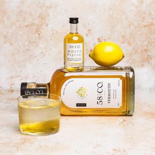 Bottle of 58 Co Vermouth with a glass of white negroni cocktail and lemon on a textured surface