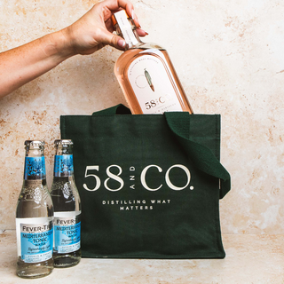 Person placing a bottle of 58 and co apple & hibiscus gin into a '58 & Co.' tote bag with two bottles of Fever-Tree tonic nearby.