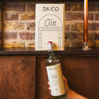 Person holding a bottle of 58 and CO Gin being refilled from a 5L BIB in front of a brick wall with a shelf displaying bottles.