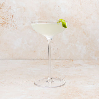 GIMLET Cocktail in a martini glass with a lime twist on a textured beige background