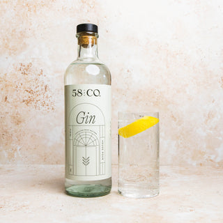 Bottle of 58 and Co Gin with a glass containing a gin and tonic with lemon twist on a textured surface
