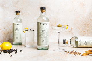 Two bottles of 58 and Co Gin on a table with a glass and garnishes, against a neutral background.