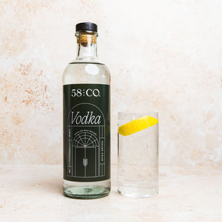 Bottle of 58 and CO Vodka with a glass containing a lemon slice on a textured surface