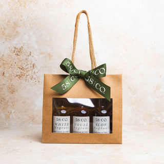 Gift set with three bottles of 58 and CO. mini negroni in a brown bag with a green ribbon on a beige background.