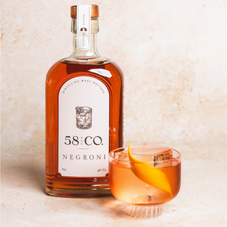 Bottle of 58 AND Co Negroni with a glass of NEGRONI on a textured surface