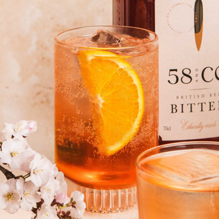 Glass of Americano cocktail with an orange slice and bottle of 58 and CO Bitter in the background.