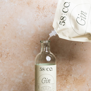 58 and Co Gin bottle being filled from a refill pouch with '58 Co Gin' branding on a beige stone background.