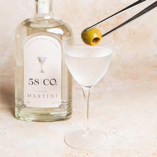 Bottle of 58 and CO Vodka Martini with a cocktail glass and olive on a light background
