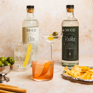 Two bottles of 58 and CO House Pour Gin and Vodka on a counter with cocktails and snacks.