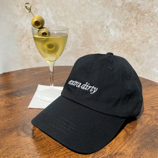 58 and CO Black cap with 'extra dirty' text next to a dirty martini cocktail on a wooden table.
