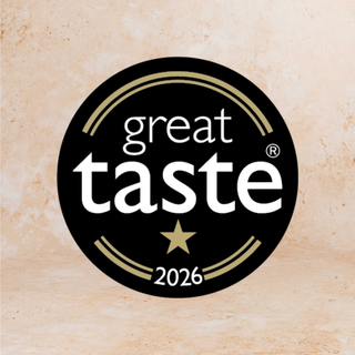 A circular black badge with the words 'great taste' in white, a gold star, and '2026' at the bottom, centered on a warm beige textured background.