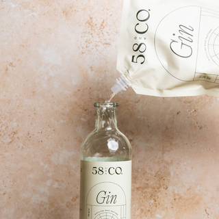 Bottle of 58 and Co House Pour Gin being filled from a refill pouch on a beige background
