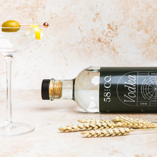 Bottle of 58 & Co. House Pour Vodka with a martini glass and wheat on a marble surface