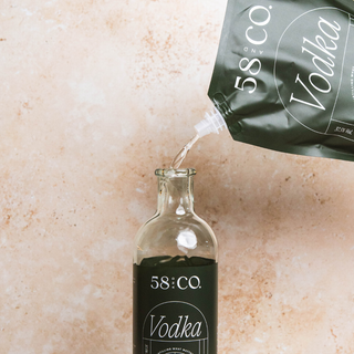 58 and Co House Pour Vodka being refilled from a refill pouch into a glass bottle on a beige background
