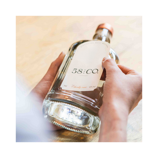 Hand labelling a bottle of 58 and Co. gin on a wooden surface