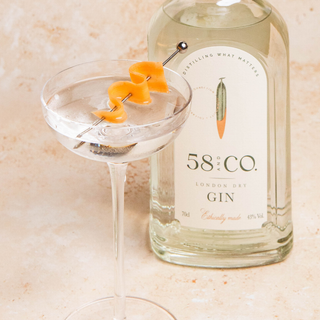 Bottle of 58 and CO London Dry gin with a martini cocktail glass containing a pickled carrot ribbon garnish on a light background