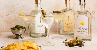 Three bottles of 58 and CO Gin, Vodka and Olive Oil Vodka with martini cocktails and garnishes on a beige textured background