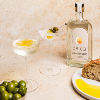 Bottle of 58 and CO Olive Oil Vodka with cocktails and olives on a table.