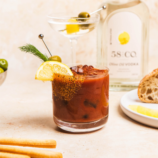 Bloody mary cocktail with lemon wedge and olives, 58 and CO olive oil vodka bottle in the background