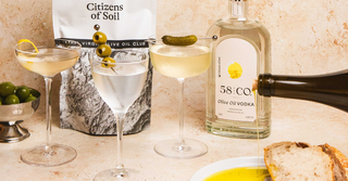 Citizens of Soil Olive Oil Pouch, a bottle of 58 and CO Olive Oil Vodka and martini cocktails with snacks and olive oil being poured onto a plate
