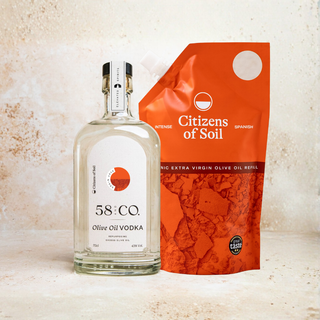 A bottle of 58 and CO. Olive Oil Vodka stands next to an orange refill pouch labeled Citizens of Soil, set against a textured light beige background.