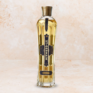 A bottle of St-Germain elderflower liqueur, set against a textured beige background.