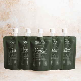 Five mini travel pouches of 58 and Co House Pour Vodka on a beige background.